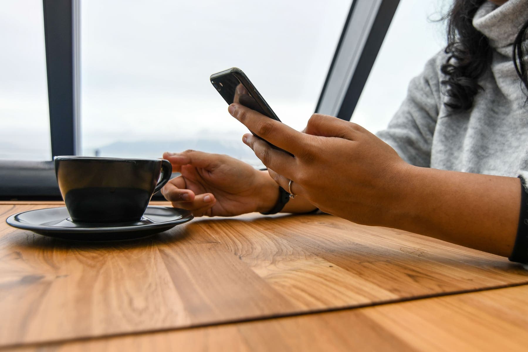 Persona revisando su celular junto a una taza de café